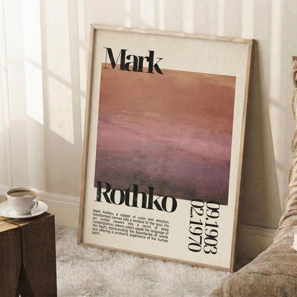 May include: Framed art print leaning against white wall in cozy room setting. Poster features abstract gradient painting in warm coral, pink and purple horizontal bands with "Mark Rothko" text overlay and exhibition details. Light wood frame, positioned next to wooden stool with white coffee cup, textured cream rug, and soft natural lighting creating window shadows on walls.