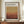 May include: Framed exhibition poster featuring Mark Rothko's name and gallery information above abstract color field artwork in warm earth tones - golden yellow transitioning to coral and deep burgundy horizontal bands. Brown wooden frame displayed on walnut credenza beside white ceramic vase and stacked books against cream paneled wall.