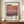 May include: Framed poster featuring abstract gradient artwork in warm coral, pink and purple tones with "Mark Rothko" text and exhibition details. Wood-framed print displayed on walnut credenza beside white ceramic vase and stacked books in elegant room with cream walls and classical molding.