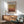 a living room with a framed poster of Mark Rothko's artwork hanging on the wall, a wooden cabinet, a green armchair, and a round wooden table.