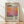 May include: Framed art print featuring Mark Rothko's name in bold black text above a gradient abstract painting with orange, pink, and purple hues. Below the artwork are dates and descriptive text about the artist. The print has a cream-colored background and sits in a light wood frame, leaning against a white wall on light wooden flooring with soft natural lighting casting shadows.