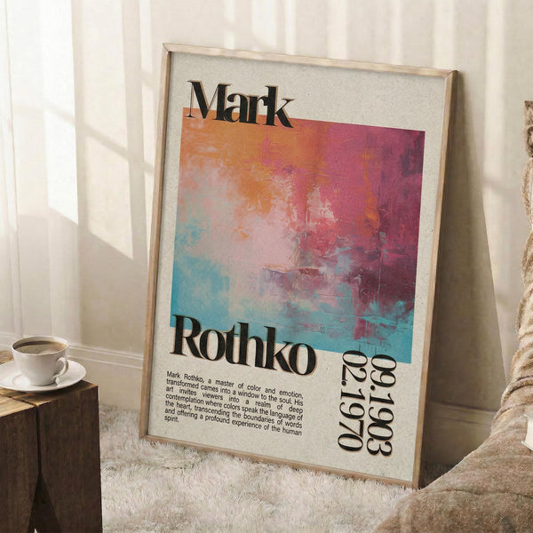 May include: Framed art print featuring abstract colorful brushstrokes in pink, orange, blue and purple tones with "Mark Rothko" text and exhibition dates. Light wood frame leaning against white wall near window with natural lighting. White coffee cup on saucer sits on wooden surface beside woven throw blanket on fluffy white rug.