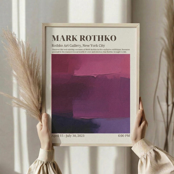 May include: Person holding framed art poster featuring abstract burgundy and purple color blocks in Rothko style, with exhibition text at top and dates at bottom. Light wood frame, neutral beige clothing, dried pampas grass visible, soft natural lighting against cream curtained background.