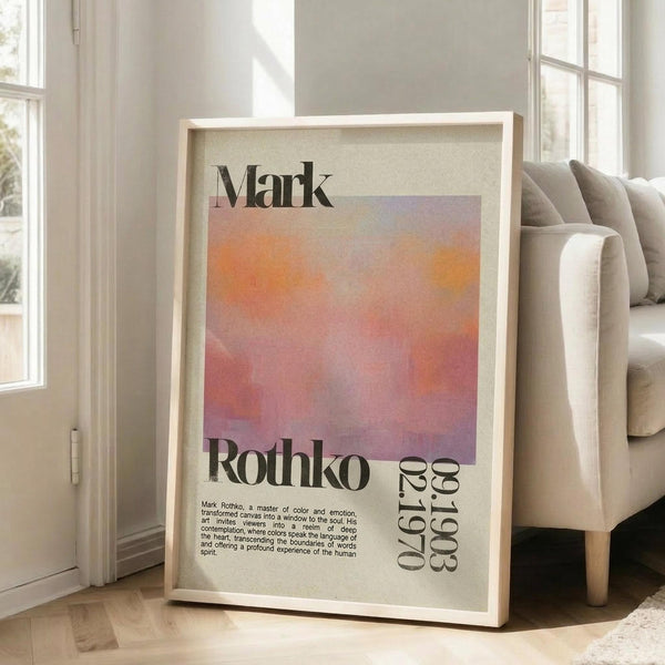 May include: Framed art print leaning against white wall beside beige couch in bright living room with large windows. The poster features abstract orange and pink gradient colors with "Mark Rothko" text and descriptive paragraph below. Light wood frame, approximately 2-3 feet tall, positioned on light wooden floor with natural sunlight streaming across the space.