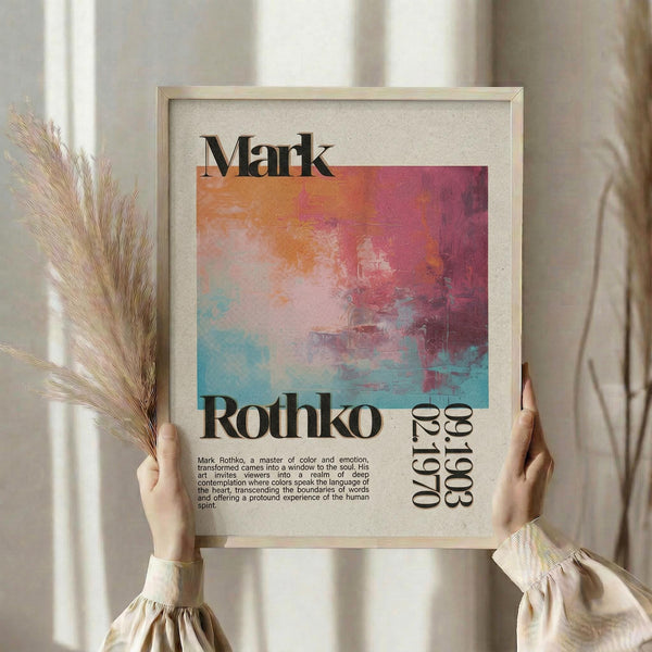 May include: Hands holding a framed abstract art print in warm light near a window. The poster features colorful brushstrokes in orange, pink, blue and turquoise tones with black typography reading "Mark Rothko" and dates "09.17.30 - 08.08.68". Small descriptive text appears below the artwork. Dried pampas grass visible on the left side, cream curtains in soft window lighting.