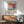 a living room with a framed poster of an abstract painting hanging on the wall, a wooden cabinet, a green armchair, and a round wooden table.