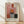 May include: Framed abstract art print featuring geometric color blocks in warm tones - pink, orange, burgundy, gray, and dark green rectangles arranged in vertical composition. Wooden frame with white matting sits on light wood floor against white wall with diagonal shadow patterns from window light.
