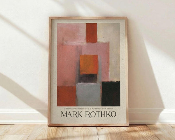 May include: Framed abstract art print featuring geometric color blocks in warm tones - pink, orange, burgundy, gray, and dark green rectangles arranged in vertical composition. Wooden frame with white matting sits on light wood floor against white wall with diagonal shadow patterns from window light.
