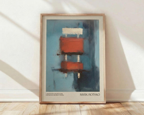 May include: Framed abstract painting poster in wooden frame with white matting, leaning against white wall on light wooden floor. Artwork shows blue-toned background with geometric red-orange rectangular shapes and white accents in painterly style. Natural window light creates soft shadows across the scene.