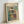 May include: Framed abstract art print leaning against white wall, featuring geometric squares and rectangles in muted teal, orange, yellow and gray tones with black linear elements. Light wood frame surrounds cream-colored background with French text "L'abstraction émotionnelle à la manière de MARK ROTHKO" above the artwork. Soft natural lighting creates subtle shadows on minimalist white surface.