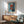 May include: Abstract art poster with blue background and red geometric shapes in wooden frame, displayed above wooden credenza with white table lamp, next to mint green mid-century modern armchair with wooden arms in bright, sunlit room with white walls.