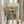 May include: Person holding framed abstract art print featuring geometric squares and rectangles in muted tones of teal, orange, yellow, and burgundy with soft brushwork and black linear elements. Light wood frame against neutral wall with dried pampas grass visible on left side. Hands wearing cream colored long sleeves with gathered cuffs.