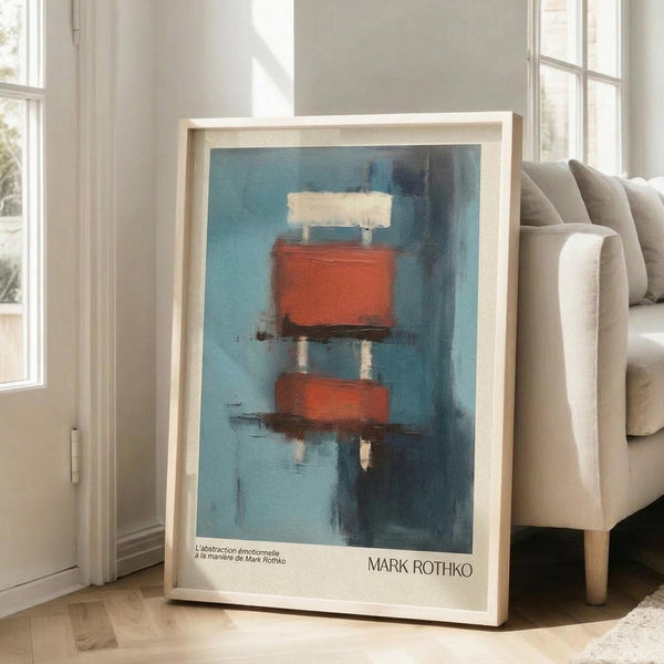 May include: Framed abstract art print in light wood frame leaning against white wall next to beige upholstered sofa. Artwork features blue-teal background with stacked red-orange and cream colored rectangular forms with vertical white lines, creating reflective water-like effect. Print has white border with "MARK ROTHKO" text at bottom. Bright natural light streams through tall windows in minimalist living room setting.