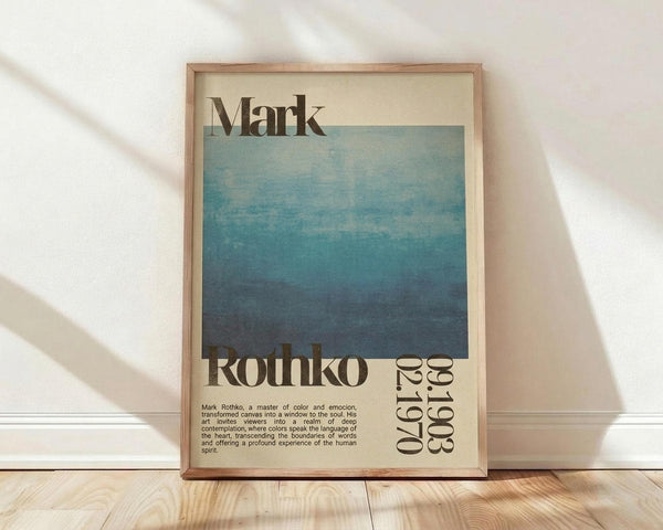 May include: Framed poster featuring Mark Rothko's name in bold black letters at top, large blue gradient square transitioning from light blue-green at top to deep navy at bottom, "Rothko" and "1903-1970" text at bottom with descriptive paragraph about the artist's work, displayed in light wood frame leaning against white wall on wooden floor with soft window light shadows