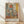 May include: Framed abstract art poster in wooden frame leaning against white wall on light wood floor. Artwork features geometric shapes in muted colors - coral, sage green, yellow, and beige tones with soft, painterly textures. Soft natural lighting creates diagonal shadows across the scene.