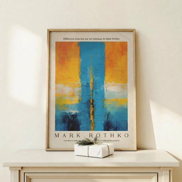 May include: Framed abstract art print with bold blue vertical brushstroke on warm orange and yellow background, displayed on light wood console table beside small white wrapped gift with twine and greenery, against cream wall in minimalist interior setting.