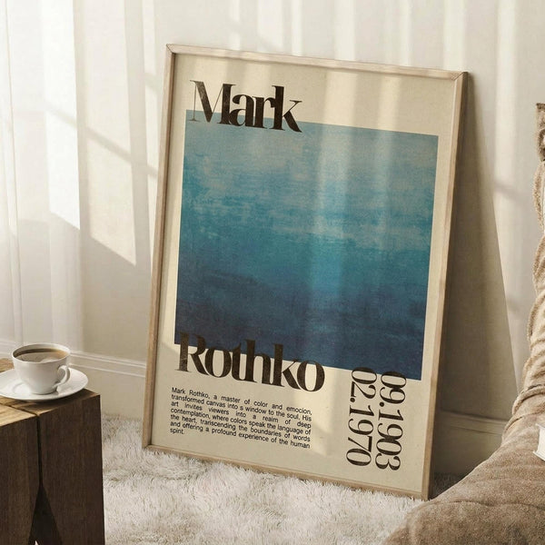 May include: A framed Mark Rothko exhibition poster featuring a blue gradient watercolor wash transitioning from light to deep blue, with black text displaying "Mark Rothko" and exhibition dates "02.19.1970". The poster is displayed in a light wood frame, leaning against white wainscoted walls on a white textured rug. A coffee cup sits on a wooden side table nearby, with soft natural lighting creating shadows across the scene.