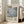 May include: Framed art poster featuring Mark Rothko's name in large serif text above a pixelated abstract composition in muted blue, gray, and teal tones. The cream-colored poster includes biographical text and dates "09.25.1903 02.25.1970" in the lower portion. The light wood frame leans against a white wall next to a beige upholstered sofa in a bright, minimalist living room with large windows and natural lighting.