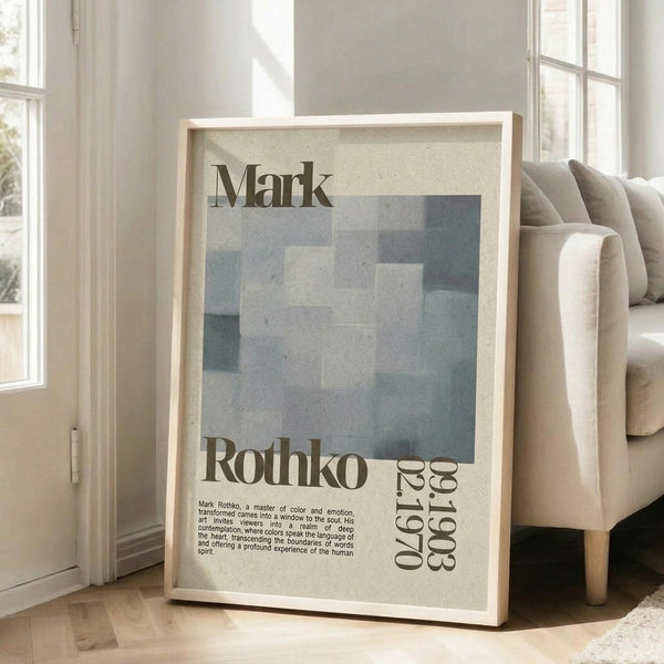 May include: Framed art poster featuring Mark Rothko's name in large serif text above a pixelated abstract composition in muted blue, gray, and teal tones. The cream-colored poster includes biographical text and dates "09.25.1903 02.25.1970" in the lower portion. The light wood frame leans against a white wall next to a beige upholstered sofa in a bright, minimalist living room with large windows and natural lighting.