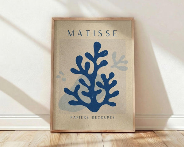 May include: Framed art print featuring blue coral-like cut-out shapes in Matisse's papiers découpés style on cream textured background, displayed in light wood frame against white wall on wooden floor with soft natural lighting and shadows.