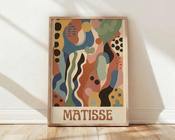 May include: Framed abstract art poster in warm earth tones featuring flowing organic shapes, dots, and curved lines in blues, oranges, greens, and coral. The composition shows flowing wave-like forms with polka dot patterns reminiscent of mid-century modern style. Text reads "MATISSE" at bottom in brown letters. Light wood frame sits against white wall on wooden floor with soft natural lighting.