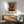 May include: Mark Rothko inspired abstract art poster with red, orange, and black rectangular color blocks on cream background, displayed in wooden frame above mid-century modern credenza. Scene shows sage green upholstered armchair with wooden arms, white ceramic table lamp, and round coffee table in sunlit room with white walls and natural shadows.