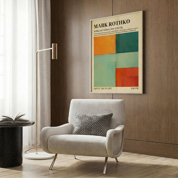 May include: A cream-colored exhibition poster featuring Mark Rothko's name and colorful abstract rectangular blocks in orange, teal, mint green, and coral red, displayed in a light wood frame on a walnut-paneled wall above a beige upholstered armchair with geometric throw pillow, beside a brass floor lamp and black side table in a modern living room setting.
