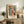 May include: Colorful abstract art print with organic shapes in blues, oranges, greens, and coral tones, featuring flowing lines and dotted patterns in the style of mid-century modern art. Framed in light wood and displayed on a rustic wooden sideboard alongside a fern plant, ceramic vase, and books in a cozy living room setting with neutral walls and warm lighting.