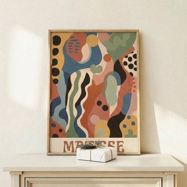 May include: Abstract colorful poster with flowing organic shapes in blue, coral, green, yellow and black dots displayed in light wood frame on white wooden shelf. Small wrapped gift with evergreen sprig sits beside the framed artwork against cream wall.