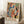 May include: A large framed poster with colorful abstract shapes in blues, oranges, greens, and yellows featuring organic forms, dots, and wavy lines in a Matisse-inspired style. The artwork leans against white paneled walls beside a wooden side table with coffee cup and blanket, displayed on a textured rug in a cozy room setting.