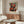 May include: Modern living room with cream chair, glass oval coffee table, and wooden sideboard. White spherical table lamp and brass floor lamp with circular shade. Framed abstract art poster on white wall featuring red and orange rectangular shapes with dark borders on blue-gray background. Clean minimalist interior with natural lighting.
