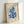 May include: Framed art print in light wood frame leaning against white wall. Poster features blue coral-like cut-out shapes on cream textured background with "MATISSE" at top and "PAPIERS DÉCOUPÉS" at bottom in navy text. Additional lighter blue organic shapes scattered around main design. Natural lighting creates soft shadows on wall.
