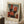 May include: Framed abstract art poster leaning against white wall on textured white rug. The artwork features geometric blocks of red-orange, gray-blue, black, and white with soft, blended edges in Rothko's signature style. Light wood frame with cream matting and French text at top. Coffee cup on wooden block nearby, beige knit throw visible at right edge.