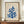 May include: Framed art print featuring blue coral-like cutout shapes in Matisse's papier découpé style on cream textured background, displayed on wooden sideboard next to white ceramic vase and stacked books in elegant room with white wainscoting and warm lighting.