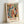 May include: Framed abstract art print in light wood frame leaning against white wall. Artwork features flowing organic shapes in coral pink, sage green, navy blue, mustard yellow, and cream with scattered dots and wavy lines. "MATISSE" text appears at bottom in brown letters. Modern minimalist styling with natural lighting casting soft shadows.