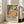 May include: Framed exhibition poster featuring Matisse-inspired artwork with vibrant tropical foliage, yellow sun, orange citrus fruits scattered on coral and blue brushstrokes. Black text below describes the artist's mastery of color and form. Natural wood frame leans against white wall next to beige sofa in bright, sunlit room with hardwood floors.