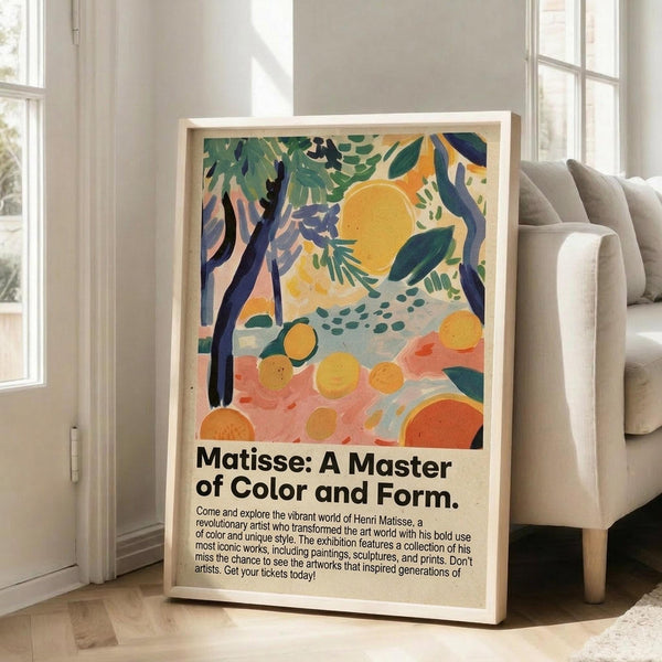 May include: Framed exhibition poster featuring Matisse-inspired artwork with vibrant tropical foliage, yellow sun, orange citrus fruits scattered on coral and blue brushstrokes. Black text below describes the artist's mastery of color and form. Natural wood frame leans against white wall next to beige sofa in bright, sunlit room with hardwood floors.