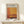 May include: Framed exhibition poster featuring Mark Rothko's name in bold black text above warm orange and brown abstract color blocks in Rothko's signature style. Light wood frame displays the poster on a white floating shelf against cream wall. Small wrapped gift with natural twine and evergreen sprig sits nearby. Soft natural lighting creates gentle shadows.