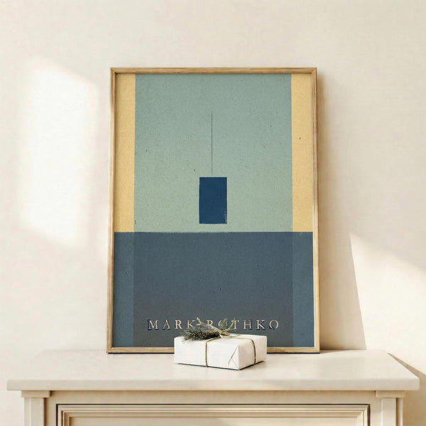 May include: Abstract minimalist artwork in wooden frame displayed on light wood surface. Composition features pale green upper section with small dark blue rectangle and thin vertical line, cream colored side panel, and darker blue-gray lower section with white text. Small wrapped gift with evergreen sprig sits nearby against neutral wall background.