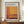 May include: Framed exhibition poster featuring Mark Rothko's abstract color field artwork in warm orange, yellow, and burgundy tones. The poster displays gallery information and exhibition dates, housed in a thin brown frame. Scene shows the artwork leaning against white wainscoted wall on a wooden credenza, styled with a cream ceramic vase and small stack of books.
