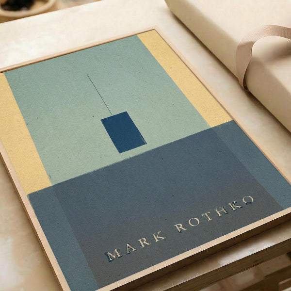 a framed artwork with a minimalist design, including a blue square and a yellow rectangle. The artwork is titled "Mark Rothko" and is displayed on a wooden surface.