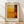 May include: Abstract art poster print in wooden frame leaning against white wall on light wood floor. Artwork features geometric blocks of warm colors - golden yellow, orange, and deep reddish-brown arranged in horizontal and vertical sections with soft, blended edges. Natural sunlight creates diagonal shadows across the white wall. Frame appears natural wood with cream matting around the artwork.