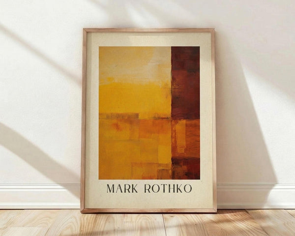 May include: Abstract art poster print in wooden frame leaning against white wall on light wood floor. Artwork features geometric blocks of warm colors - golden yellow, orange, and deep reddish-brown arranged in horizontal and vertical sections with soft, blended edges. Natural sunlight creates diagonal shadows across the white wall. Frame appears natural wood with cream matting around the artwork.