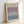 May include: Framed art exhibition poster featuring Mark Rothko's name in bold black text at top, with gallery information and exhibition dates below. The center displays a soft gradient artwork transitioning from dusty purple at top to pale blue at bottom. Light wood frame against white wall with natural lighting creating gentle shadows.