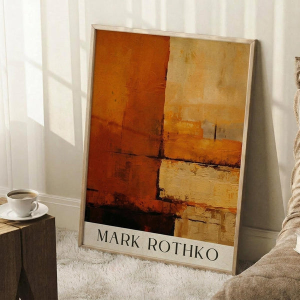May include: Abstract expressionist artwork with warm orange, rust, and cream colored rectangular blocks separated by dark brushstrokes, displayed in thin light wooden frame leaning against white wall corner. Coffee cup on wooden side table and textured cream blanket visible nearby, creating cozy interior setting with natural window light casting shadows.