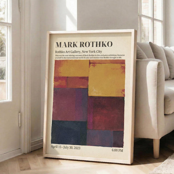 May include: Framed exhibition poster featuring Mark Rothko's abstract color field artwork in warm yellows, deep purples, burgundy, and dark blue rectangular blocks. Light wooden frame leaning against white wall next to beige upholstered sofa in bright, airy room with tall windows and natural sunlight streaming across white floors.