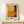 May include: Abstract art print in warm tones displayed in light wood frame on pale wooden surface. Artwork features geometric blocks of yellow, orange, and deep red colors with soft, painterly edges. Small white gift box with natural twine and greenery sits beside the framed piece against cream wall background.