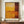 May include: Abstract art print in warm orange, yellow and deep red rectangular blocks displayed in thin brown frame on wooden sideboard. White ceramic vase and stacked books nearby. Classic interior with white paneled walls and molding visible in background.