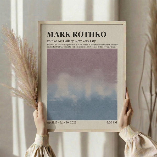 May include: Hands holding a framed art exhibition poster featuring Mark Rothko's name and a gradient artwork transitioning from purple at top to blue at bottom. Light wooden frame against cream curtains with dried pampas grass visible on left side. Poster shows gallery text and exhibition dates in minimalist typography on beige background.