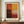 May include: Abstract color field artwork in warm tones of red, orange, yellow and cream arranged in rectangular blocks, displayed in brown wooden frame on walnut credenza beside white ceramic vase and stacked books against cream wainscoted wall